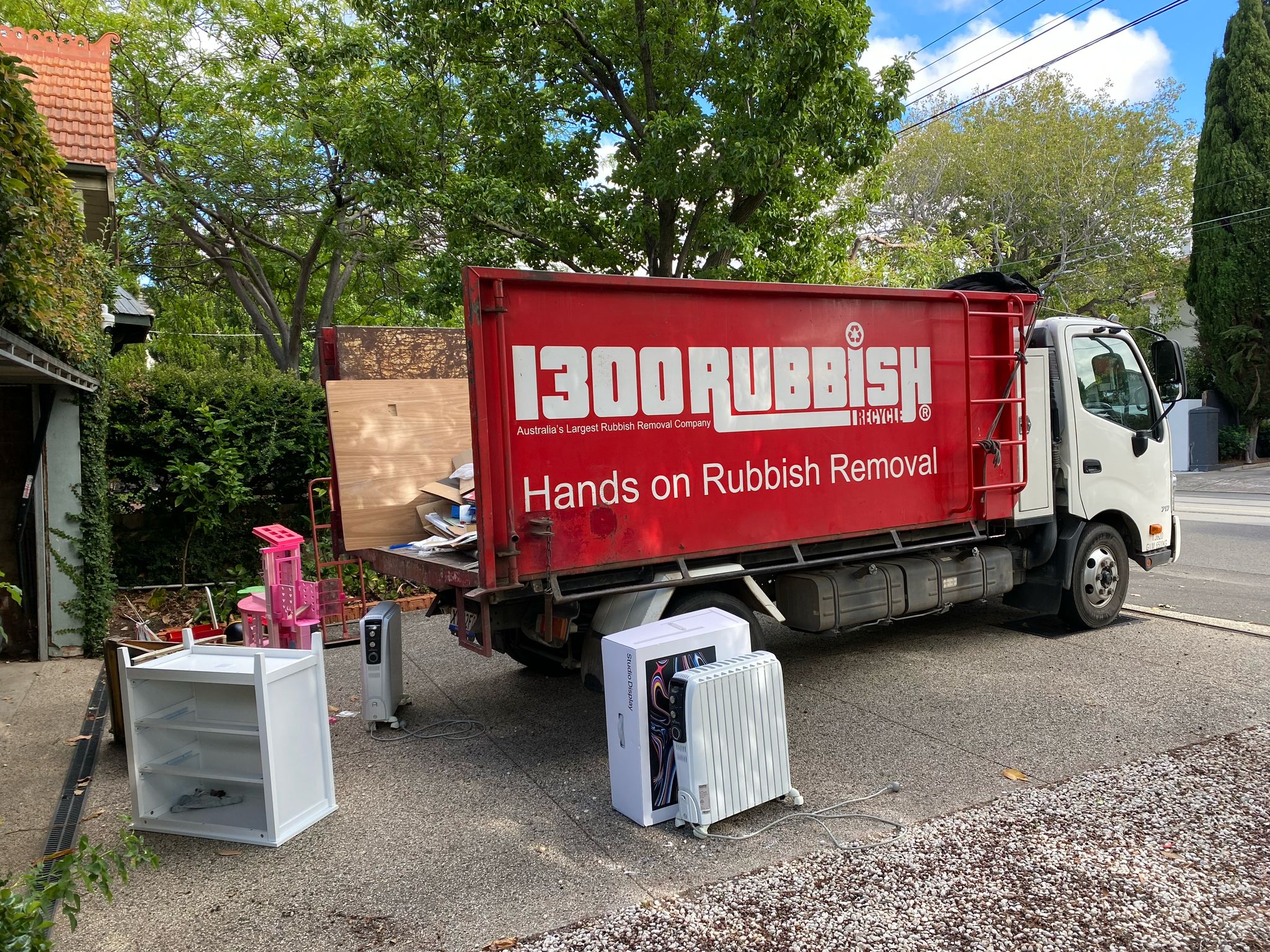 An end of lease rubbish removal in progress: a uniformed worker in red stands next to a bright red rubbish truck, carrying items out of a building to be loaded onto the vehicle.